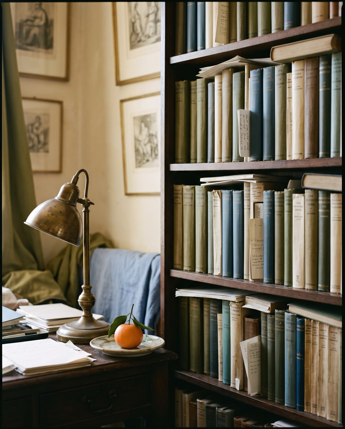 A corner of a study: a wooden bookshelf of cloth-bound books, a brass lamp, and a mandarin on a saucer